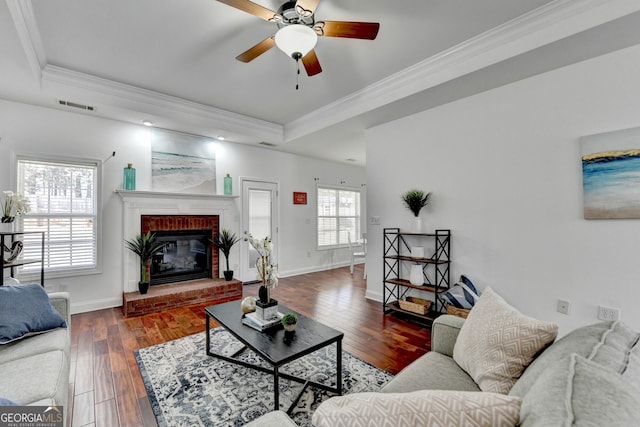 living room featuring ornamental molding, a fireplace, dark hardwood / wood-style flooring, and a tray ceiling