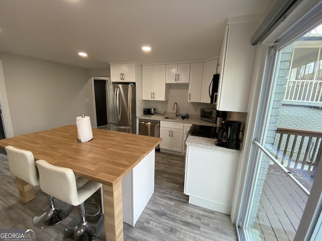 kitchen featuring appliances with stainless steel finishes, sink, white cabinets, a kitchen bar, and hardwood / wood-style flooring