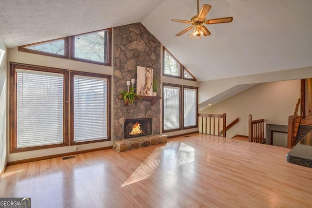 unfurnished living room featuring ceiling fan, high vaulted ceiling, a fireplace, and light hardwood / wood-style flooring