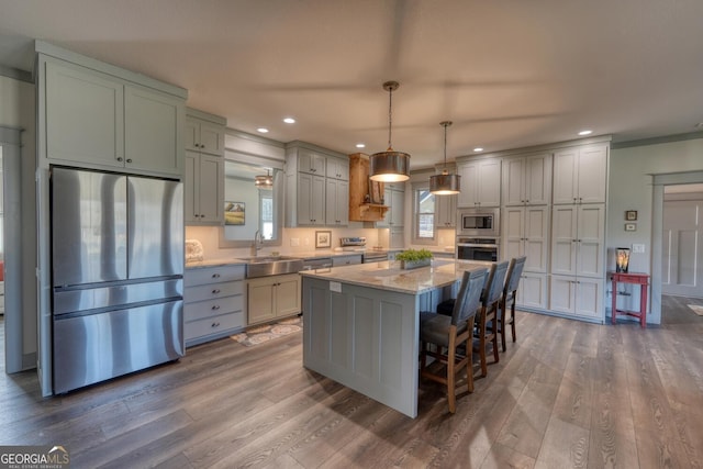 kitchen with appliances with stainless steel finishes, sink, hanging light fixtures, a center island, and light stone counters