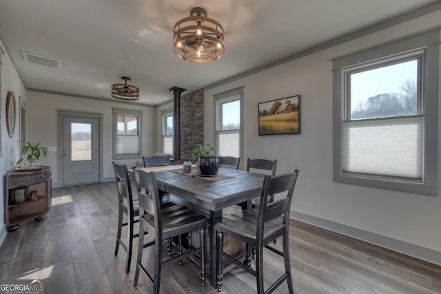 dining space with hardwood / wood-style floors, crown molding, and a wood stove