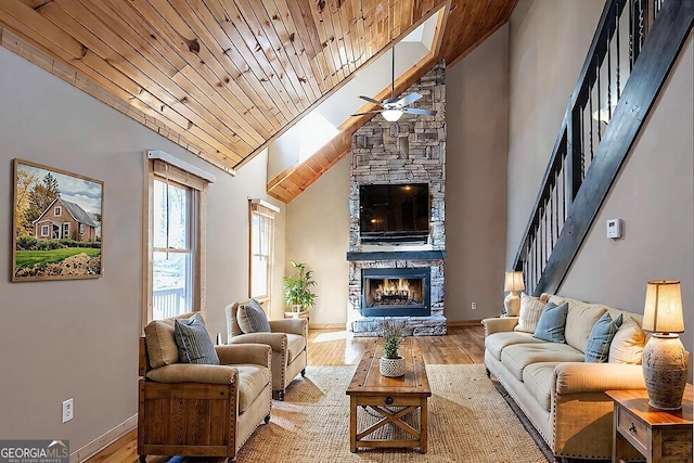 living room featuring a stone fireplace, wood-type flooring, high vaulted ceiling, wooden ceiling, and ceiling fan