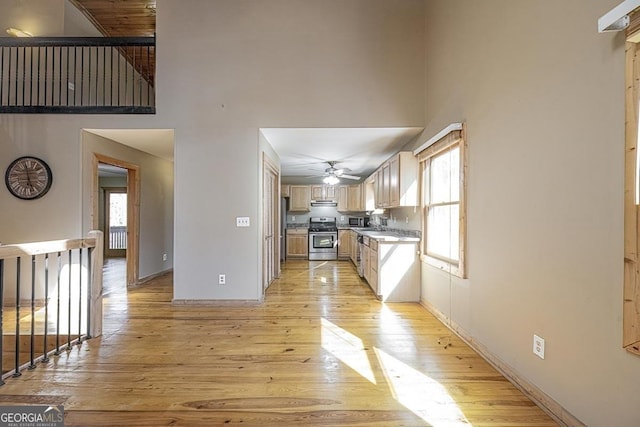 kitchen with extractor fan, appliances with stainless steel finishes, a towering ceiling, ceiling fan, and light hardwood / wood-style floors