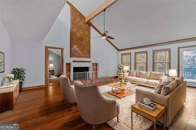 living room with a towering ceiling, wood-type flooring, ornamental molding, and ceiling fan