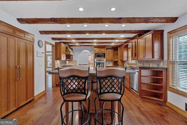 kitchen featuring dark wood-type flooring, a center island, appliances with stainless steel finishes, a kitchen breakfast bar, and decorative backsplash