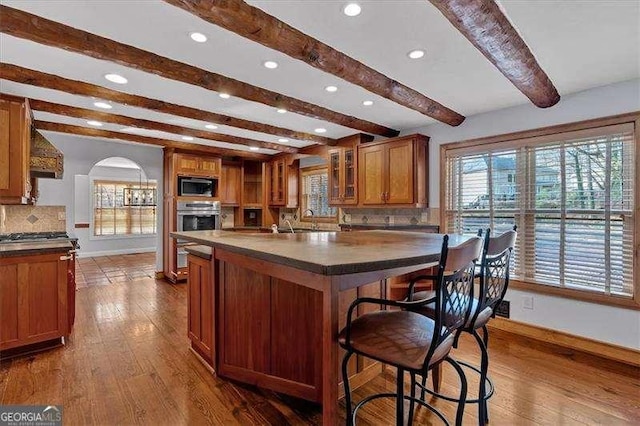 kitchen featuring dark wood-type flooring, tasteful backsplash, appliances with stainless steel finishes, a kitchen island, and beam ceiling