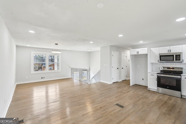 kitchen featuring white cabinetry, hanging light fixtures, appliances with stainless steel finishes, light hardwood / wood-style floors, and decorative backsplash