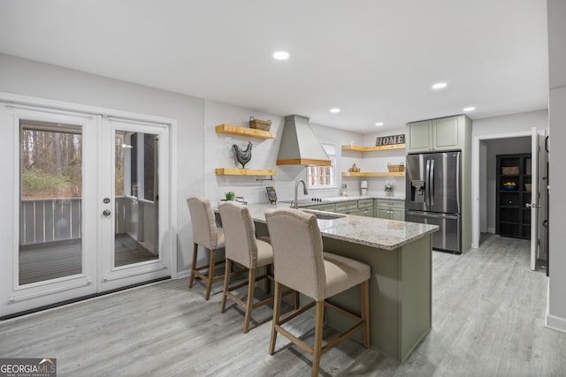 kitchen with a breakfast bar, green cabinets, stainless steel refrigerator with ice dispenser, light stone countertops, and kitchen peninsula