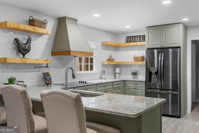 kitchen featuring a breakfast bar, stainless steel fridge with ice dispenser, custom exhaust hood, kitchen peninsula, and light stone countertops