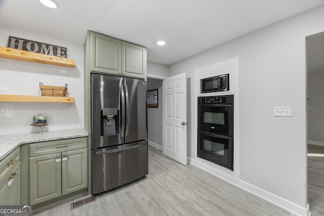 kitchen with green cabinetry, black appliances, light hardwood / wood-style flooring, light stone countertops, and backsplash