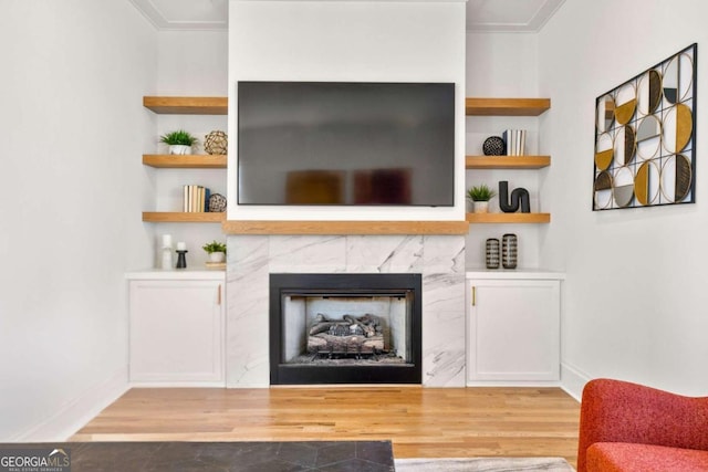 living room with built in features, a premium fireplace, and light hardwood / wood-style flooring