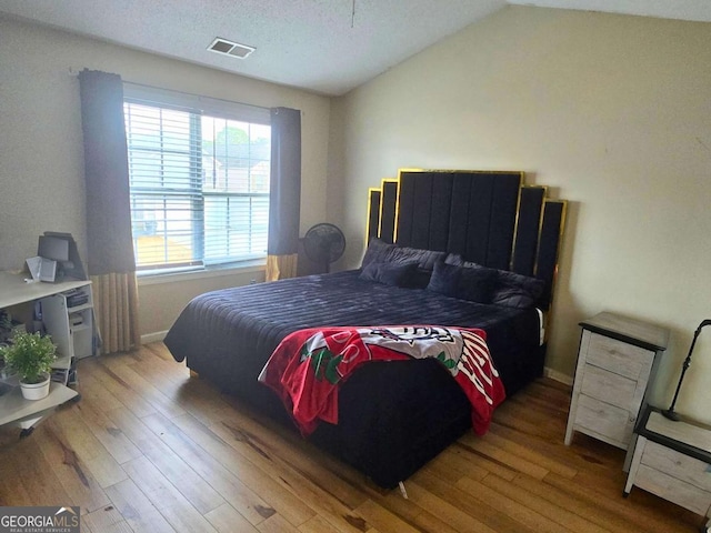 bedroom with lofted ceiling, wood-type flooring, and a textured ceiling