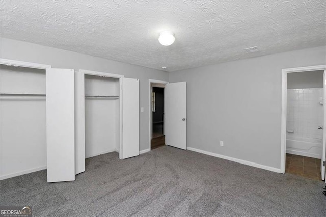 unfurnished bedroom featuring ensuite bathroom, carpet flooring, two closets, and a textured ceiling