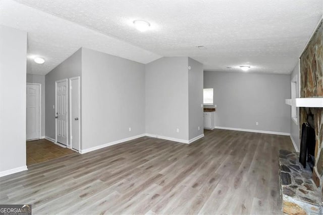 unfurnished living room featuring vaulted ceiling, wood-type flooring, a large fireplace, and a textured ceiling