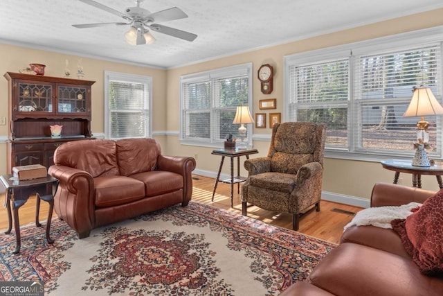 living room featuring a textured ceiling, ornamental molding, ceiling fan, and light wood-type flooring