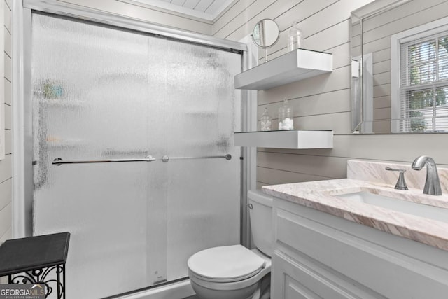 bathroom with wood walls, toilet, vanity, and a shower with shower door