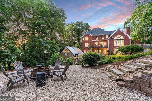 back house at dusk with an outbuilding, a balcony, and a fire pit