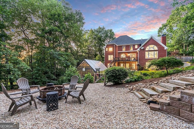 back of property at dusk with an outbuilding, a greenhouse, a balcony, a fire pit, and brick siding