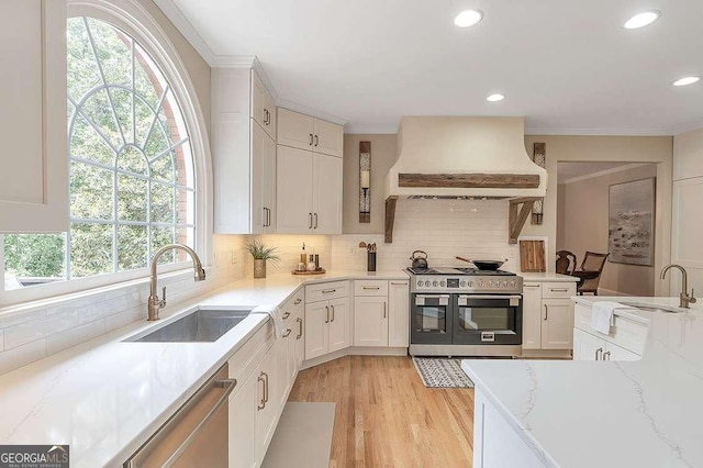 kitchen featuring sink, custom range hood, white cabinets, and appliances with stainless steel finishes