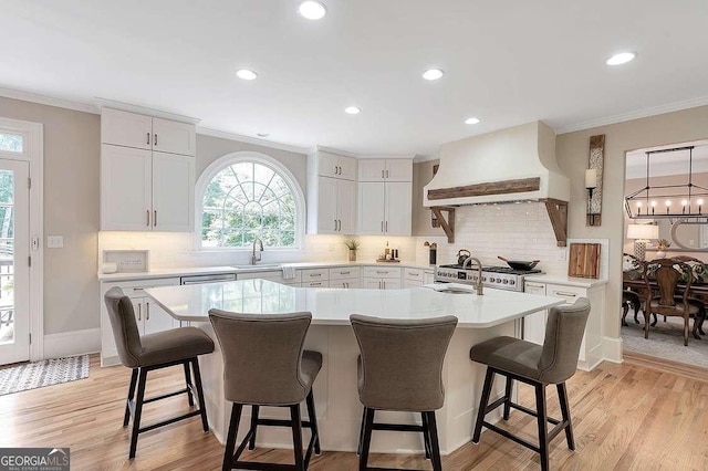 kitchen featuring custom exhaust hood, an island with sink, white cabinets, and a kitchen bar