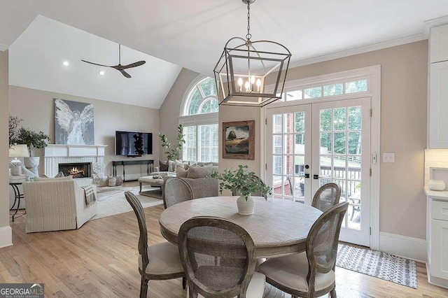 dining area with a warm lit fireplace, ceiling fan, vaulted ceiling, french doors, and light wood-style floors