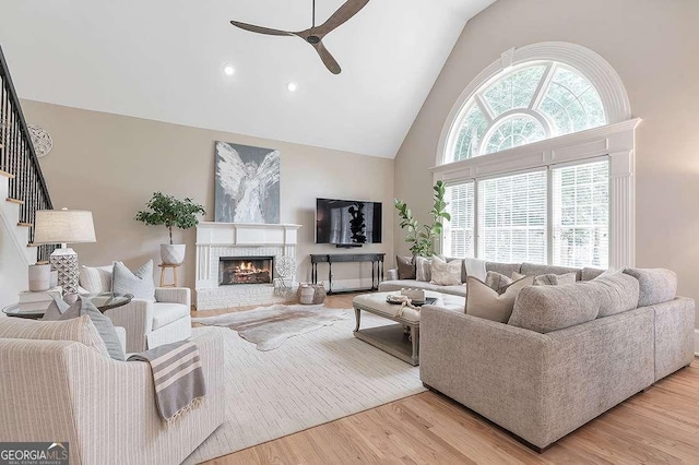 living room featuring a wealth of natural light, a brick fireplace, a ceiling fan, and light wood-style floors