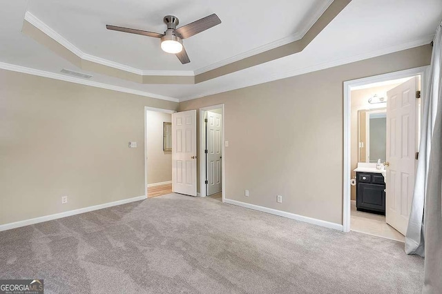 unfurnished bedroom featuring ceiling fan, a tray ceiling, crown molding, light carpet, and ensuite bath