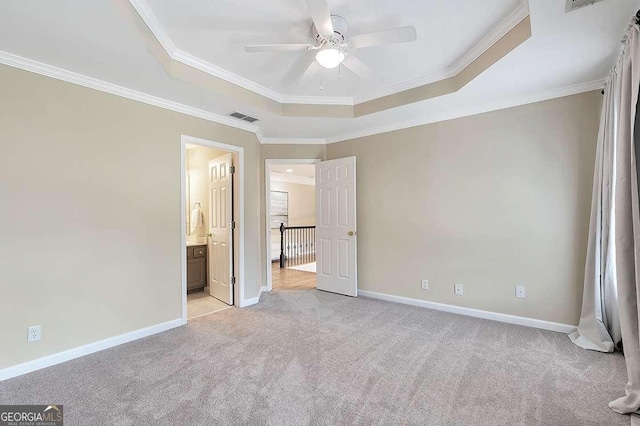 unfurnished bedroom featuring ensuite bath, ornamental molding, light colored carpet, and a raised ceiling