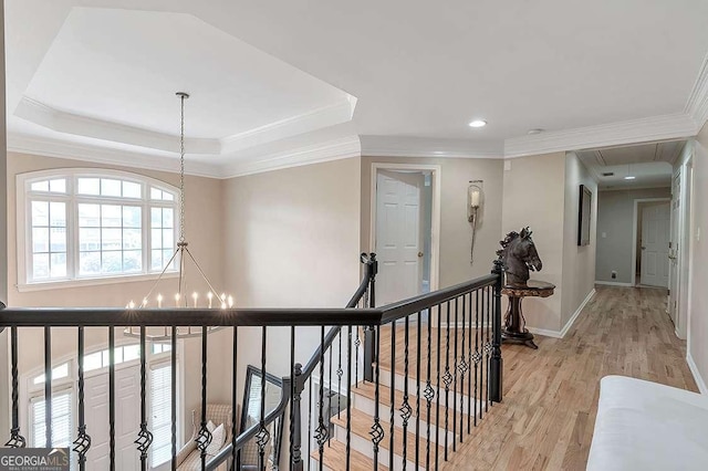 hall featuring a raised ceiling, crown molding, light wood-type flooring, and an inviting chandelier