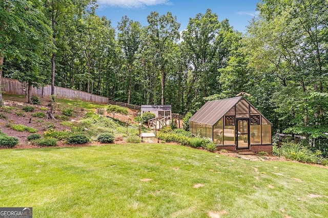 view of yard with a greenhouse, fence, and an outbuilding