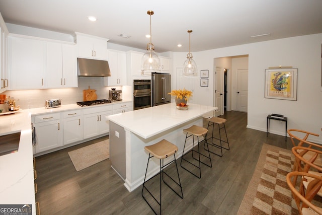 kitchen featuring under cabinet range hood, white cabinetry, light countertops, appliances with stainless steel finishes, and decorative light fixtures