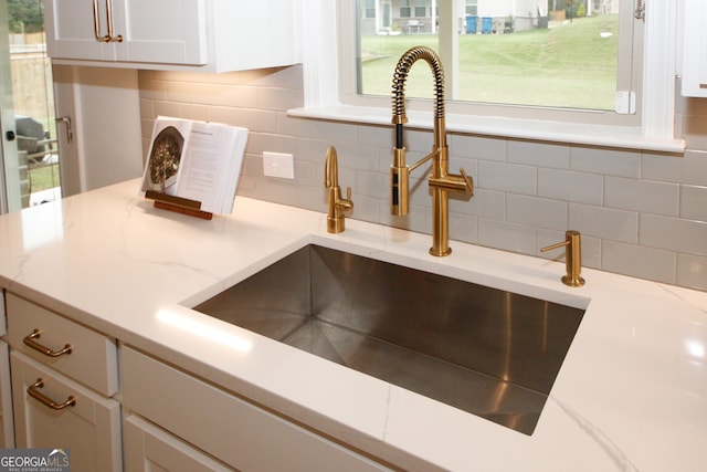 interior details with backsplash, a sink, and white cabinetry