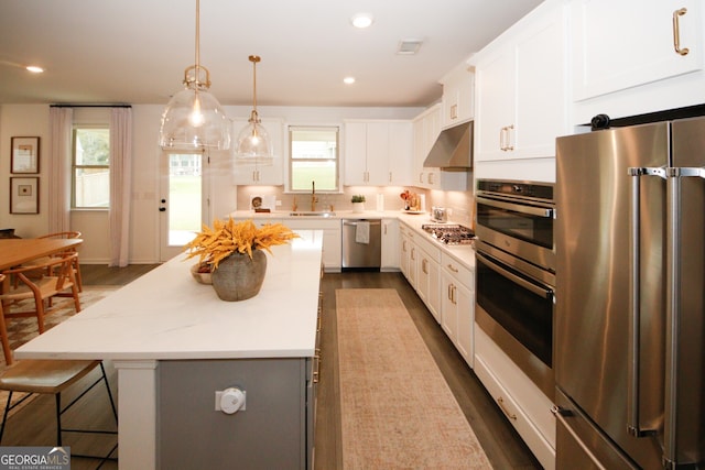 kitchen with a center island, pendant lighting, appliances with stainless steel finishes, white cabinetry, and extractor fan