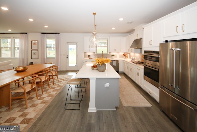 kitchen featuring under cabinet range hood, white cabinets, light countertops, appliances with stainless steel finishes, and a center island