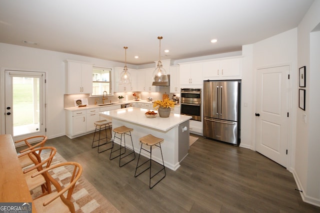 kitchen with a sink, light countertops, appliances with stainless steel finishes, hanging light fixtures, and a center island