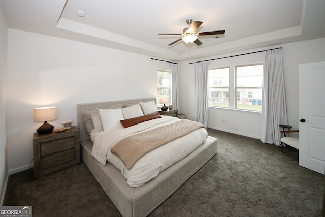 bedroom with baseboards, a tray ceiling, and dark colored carpet