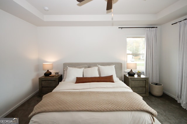 bedroom featuring baseboards, dark carpet, and a raised ceiling