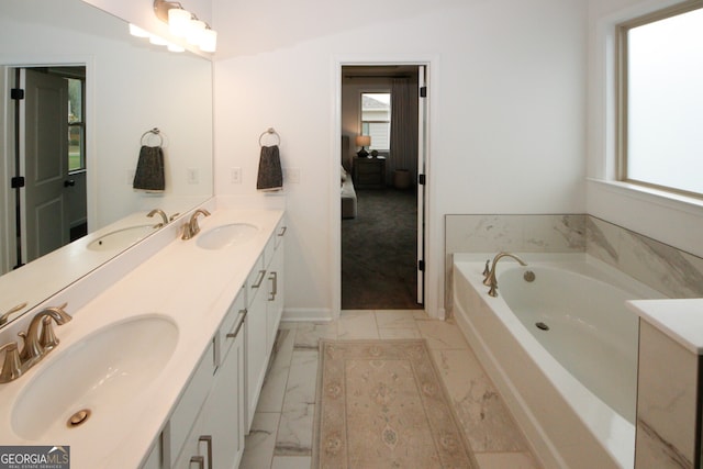 ensuite bathroom with marble finish floor, a sink, and a bath