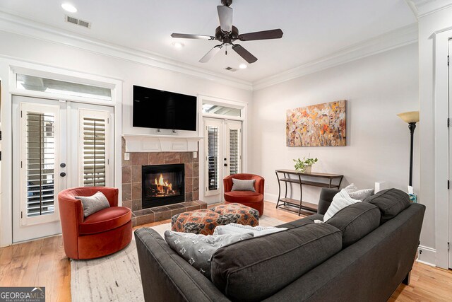 living room featuring ornamental molding, a fireplace, light hardwood / wood-style floors, and french doors