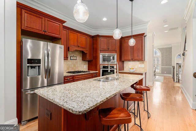 kitchen featuring sink, light stone counters, pendant lighting, stainless steel appliances, and a kitchen island with sink