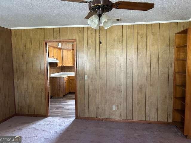 carpeted spare room with ceiling fan, ornamental molding, wooden walls, and a textured ceiling