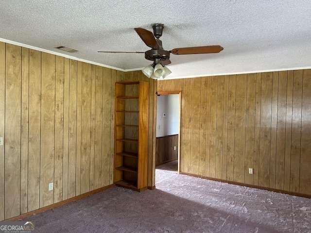 spare room featuring ceiling fan, wooden walls, dark carpet, and a textured ceiling