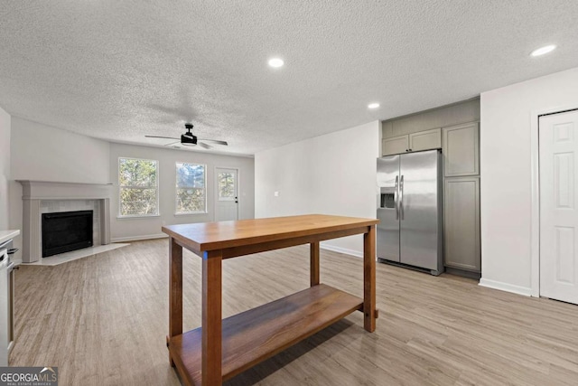 kitchen with gray cabinetry, stainless steel fridge with ice dispenser, light hardwood / wood-style flooring, a tile fireplace, and ceiling fan