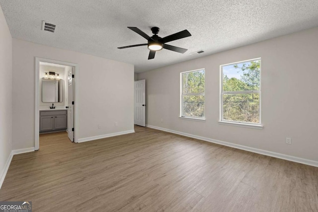 unfurnished bedroom featuring ceiling fan, ensuite bath, light hardwood / wood-style floors, and a textured ceiling