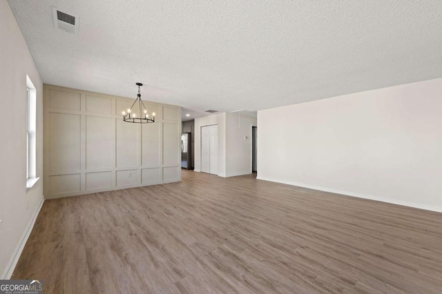 unfurnished living room featuring a notable chandelier, hardwood / wood-style flooring, and a textured ceiling