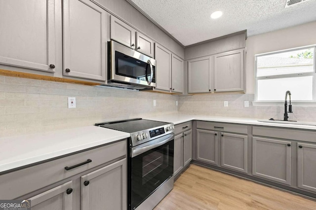 kitchen with sink, gray cabinets, stainless steel appliances, and light hardwood / wood-style floors