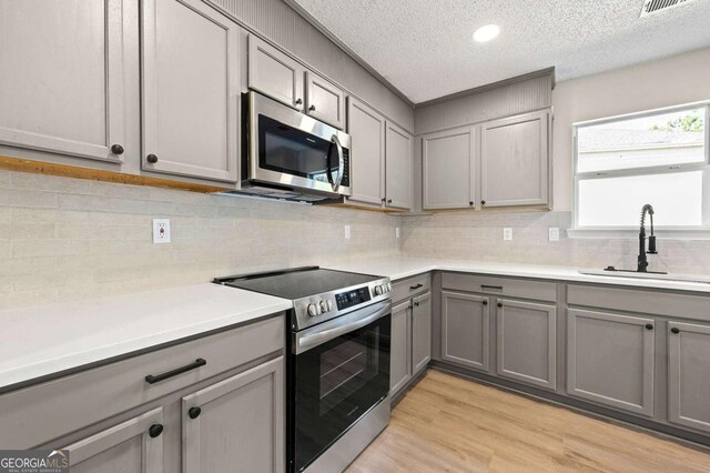 kitchen featuring stainless steel appliances, gray cabinets, and light hardwood / wood-style flooring