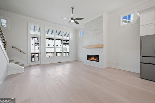 unfurnished living room with crown molding, light wood-type flooring, ceiling fan, and a fireplace