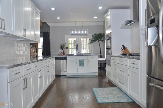 kitchen with appliances with stainless steel finishes, decorative light fixtures, white cabinets, kitchen peninsula, and wall chimney exhaust hood