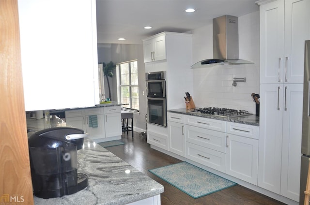 kitchen with dark wood-type flooring, white cabinetry, light stone counters, appliances with stainless steel finishes, and wall chimney range hood